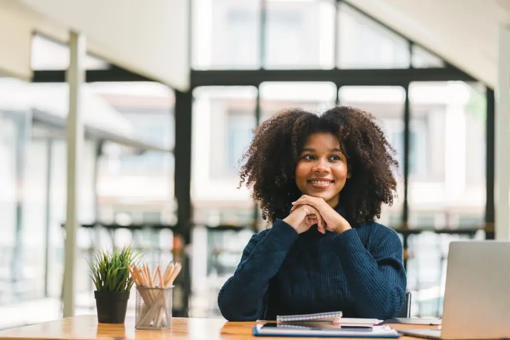 Woman sitting at a desk with a laptop, smiling while reviewing documents—representing staying informed and vigilant about protecting personal information during tax season.